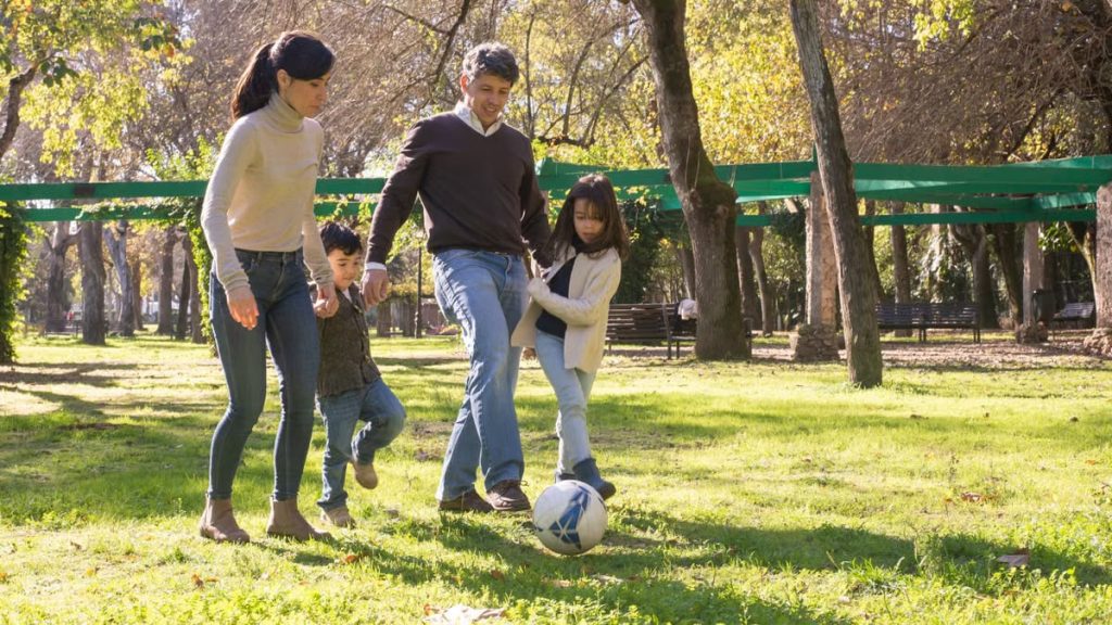 A family plays soccer together in a sunny park, enjoying quality time outdoors.
