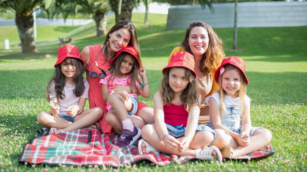 Friends enjoying a sunny day picnic on grass with bucket hats and smiles in a Portuguese park.